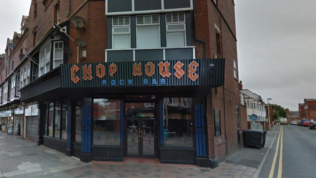 An outside view of a bar with a black corrugated sign with red and blue letters spelling out Chop House Rock Bar 