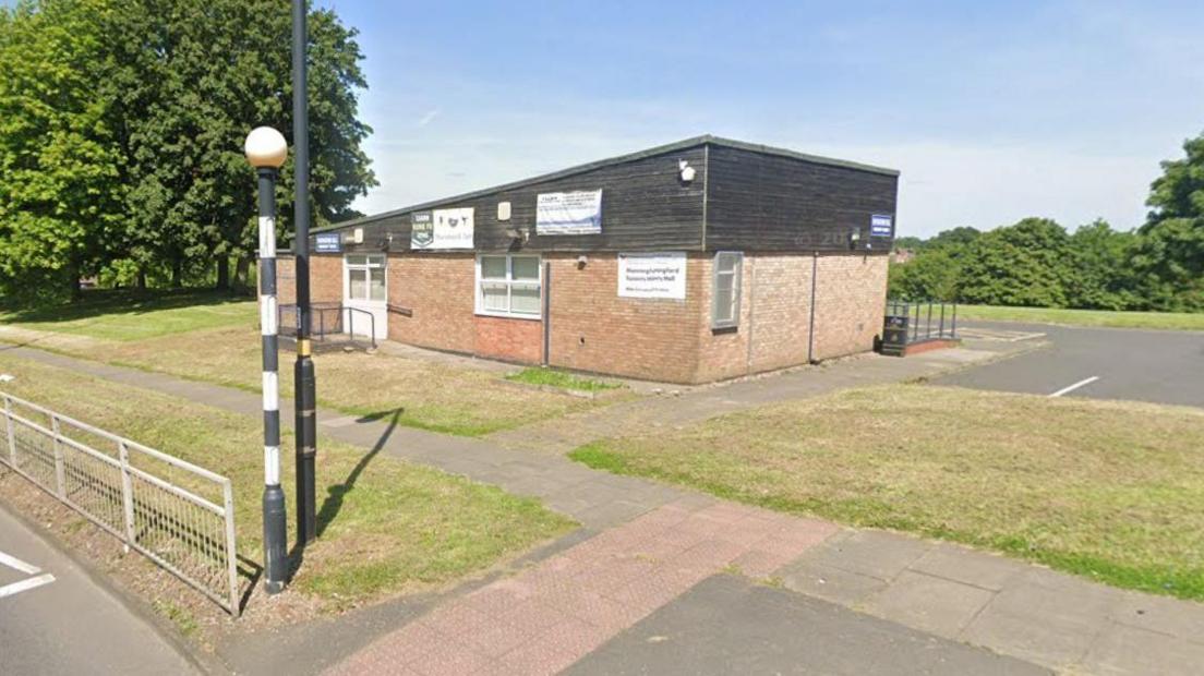 A single-storey building with a black roof, near a zebra crossing.