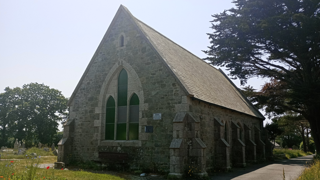 A chapel surrounded by grass and trees on a sunny day with blue skies.