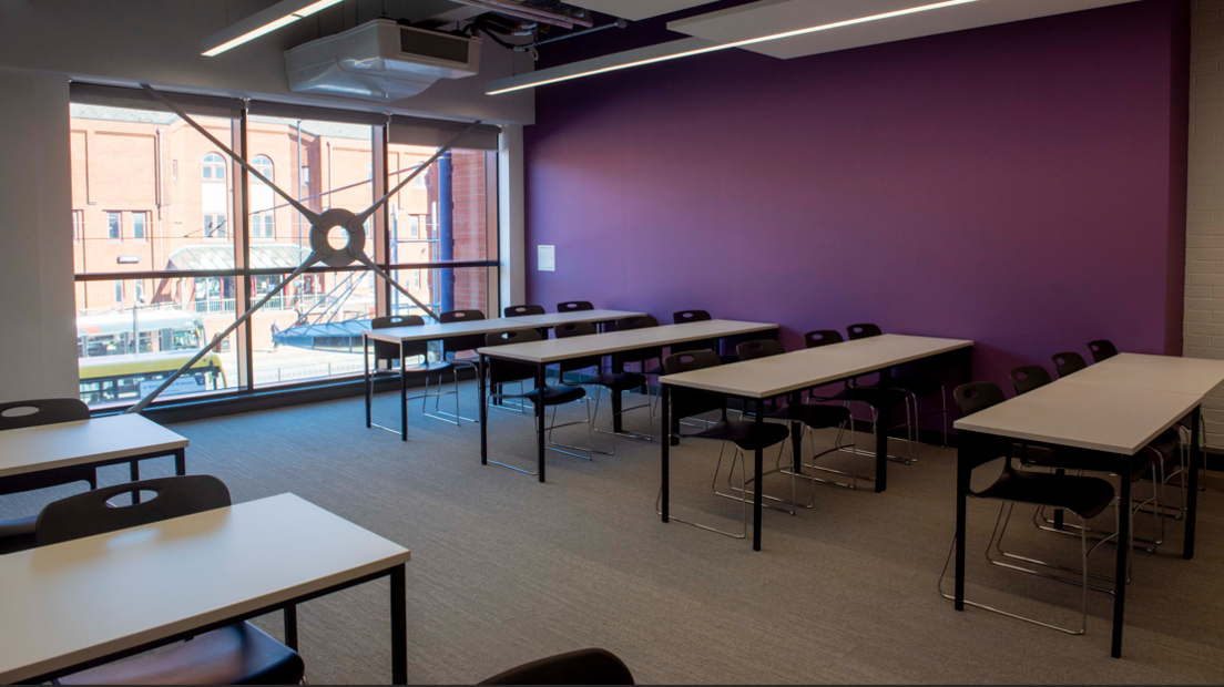 A purple painted wall section can be seen on the right of the image with sleek desks and chairs and a large glass window at the rear of the room.