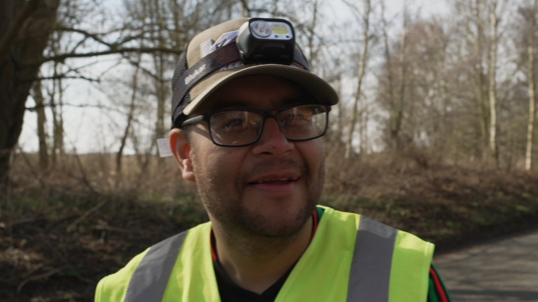 A man in glasses and hi-vis vest with a baseball cap and camera on his head