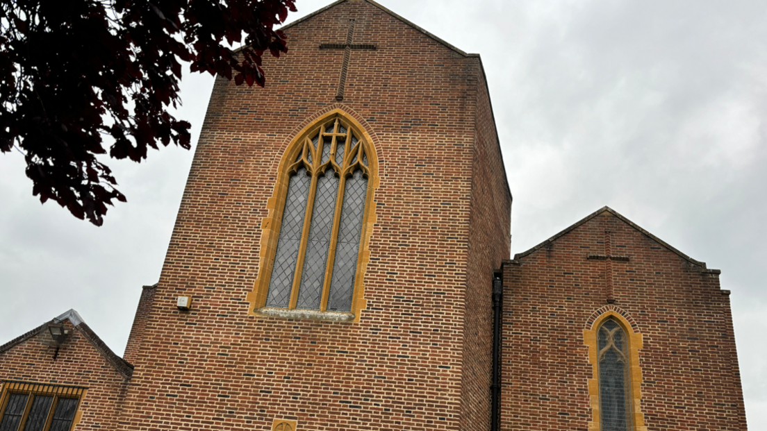 Red bricked church buildings with tall glass windows and a cross at the top