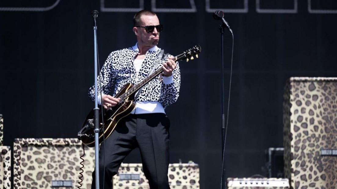 a man in a leopard print top with a guitar