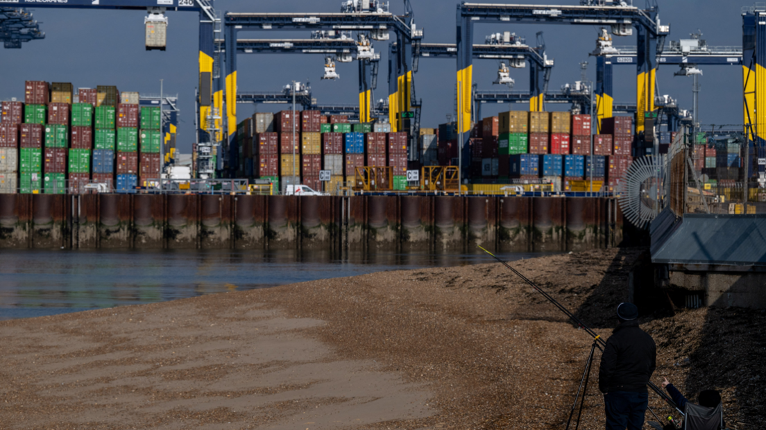 Port of Felixstowe wide showing cranes and freight with a sand bank in the foreground and a fisherman watching on