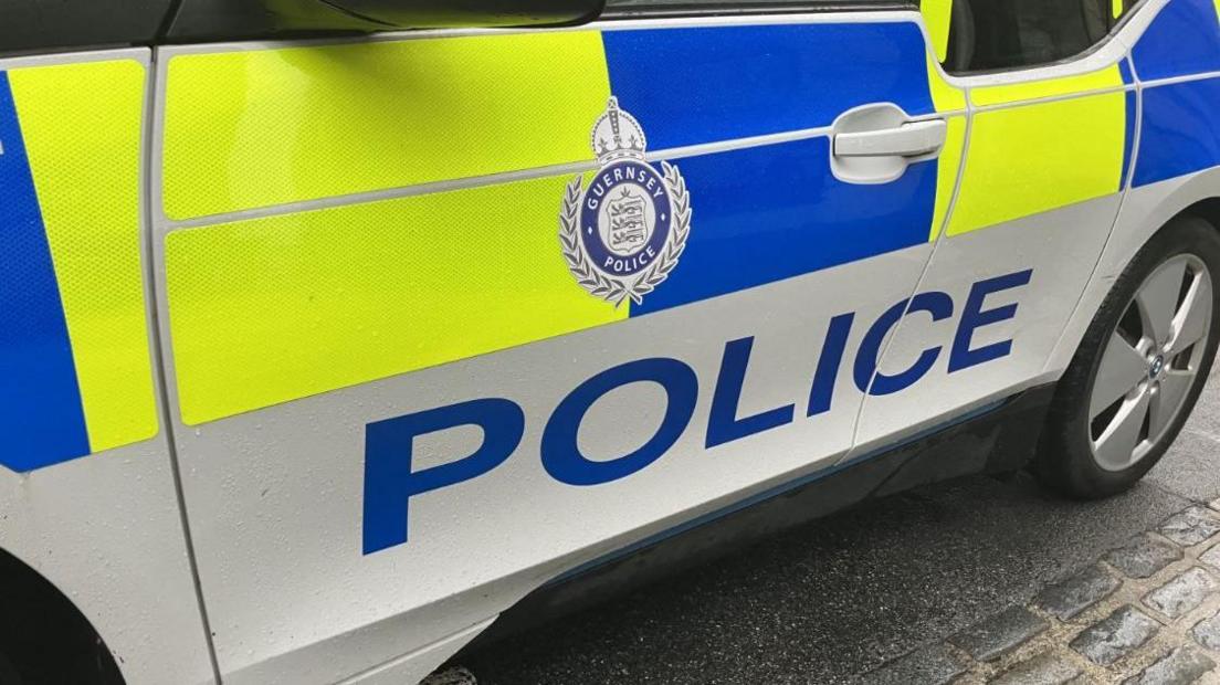 Guernsey Police car pictured. The image only shows the door which is coloured yellow, blue and white with police in blue lettering. There is also a Guernsey Police emblem on the door.