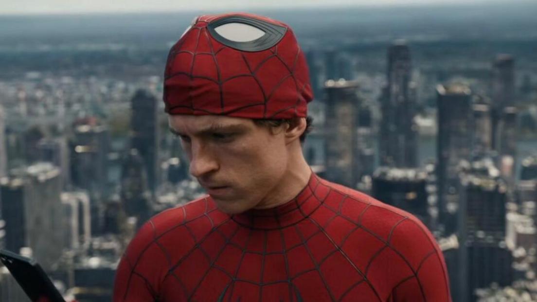 Tom Holland with his Spider-Man mask half off looks at a phone. 