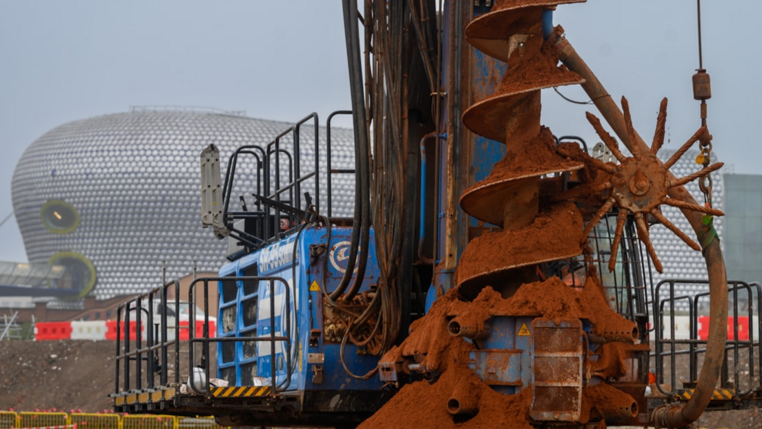 A huge drill has soil on it and stands next to large machinery with the Bullring shopping centre in the background.