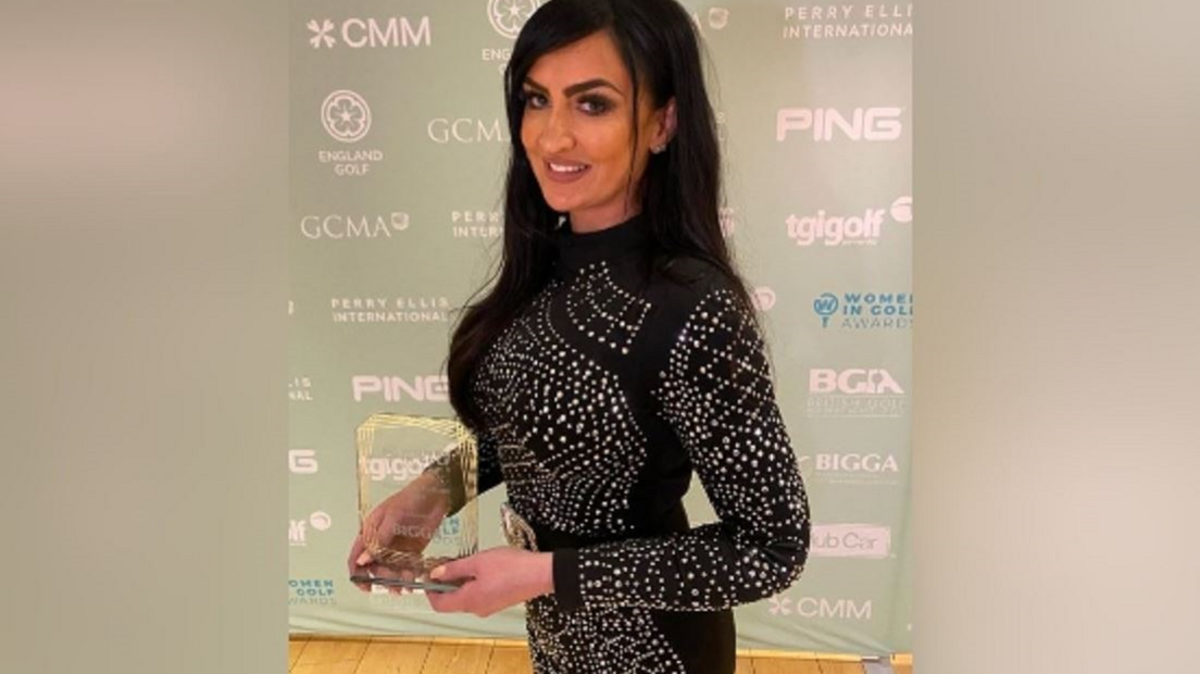 Anna is wearing a black sequinned dress and is holding her award. She has long dark hair and make-up on.