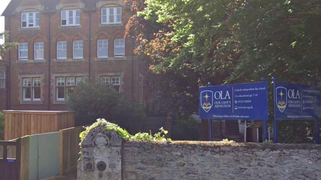 Outside Our Lady's Abingdon on  a sunny day. Blue school signs are installed in front of the building.