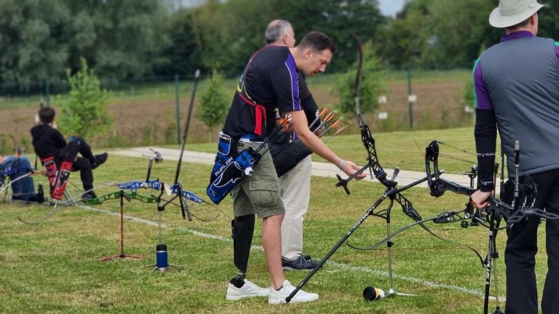 Richard Davies, who has a prosthetic leg, gets his bow ready for action while dressed in green shorts and sports top.