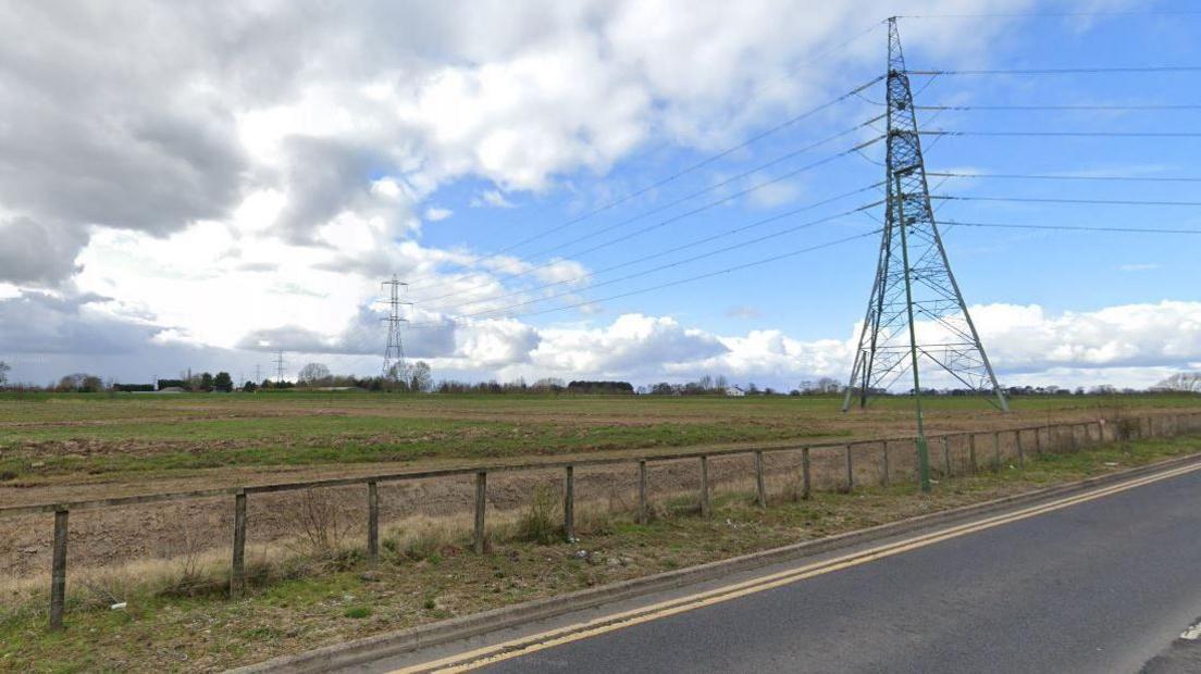 The site where the homes are due to be built. The picture shows a field with a line of pylons crossing it. 