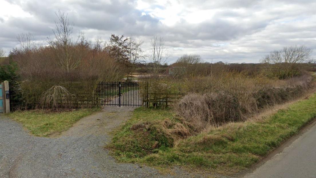 Street view of a gravel path, bordered by greenery with a black gate in the middle