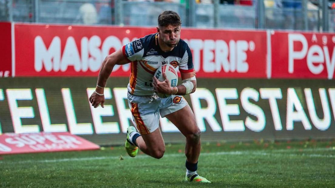 Tommy Makinson running towards the line with the ball in his left hand for Catalans Dragons.
