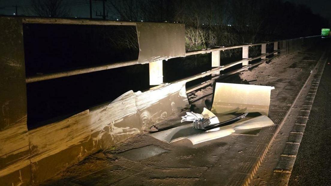 A damaged white barrier that lies next to a road has had panels fall off of it.