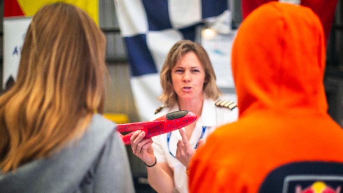 A female pilot holds a model plane while she talks to two girls