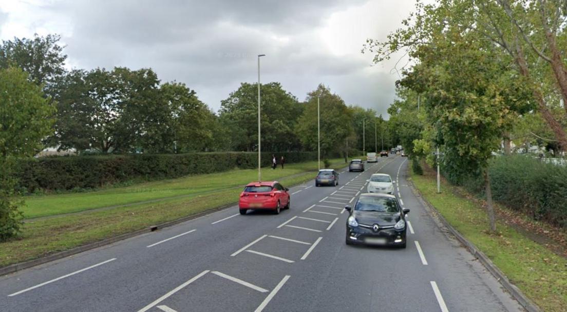 Cars driving in both directions on Cole Avenue in Gloucester, which is bordered on both sides by grass, hedges and trees on a cloudy day