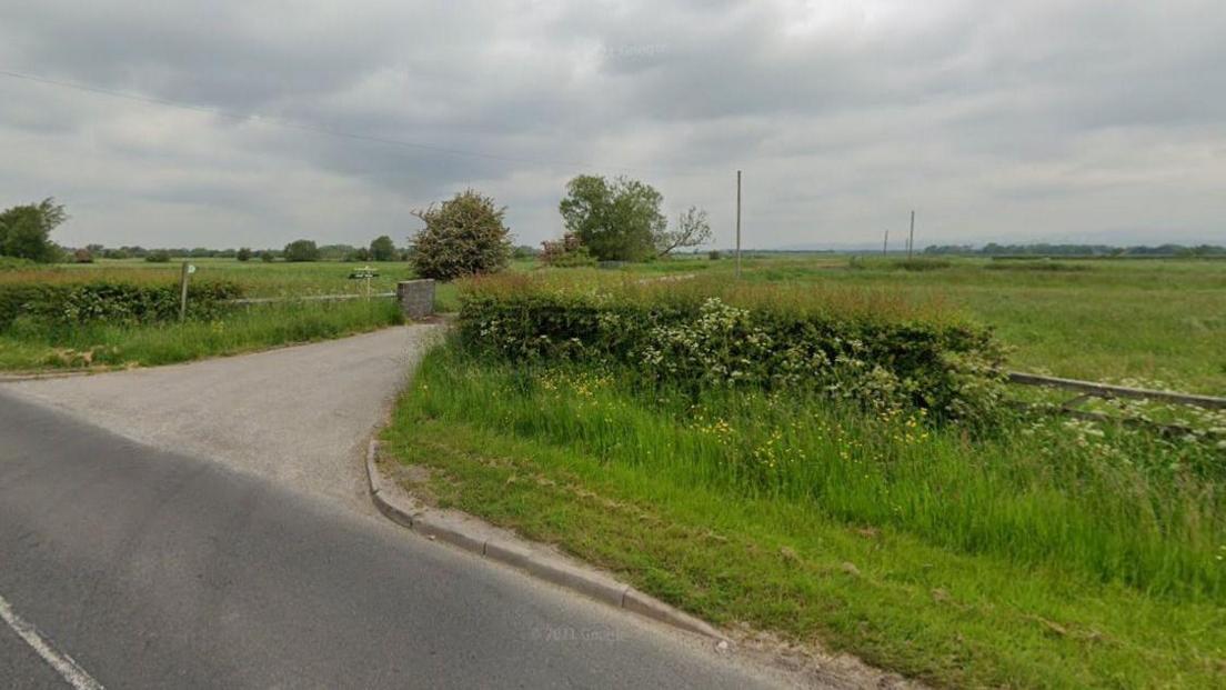 The entrance to the farm can be seen, with trees in the distance.