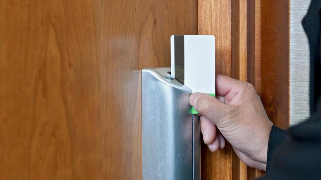 A hand swiping a magnetic keycard through a door lock