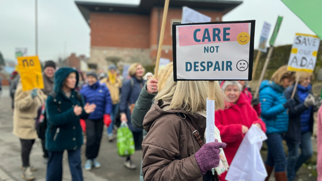 Campaigners holding placards and marching through the streets of Belper. Placards read "Care not despair" and "Save our Ada"
