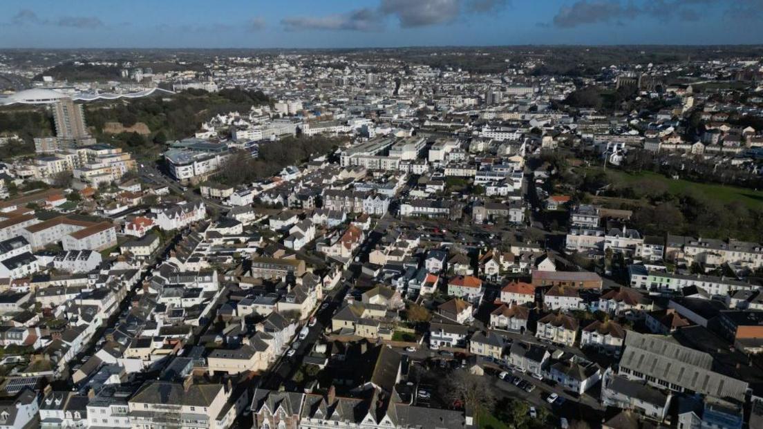 An aerial shot of a town with houses, other buildings and fields dotted around.