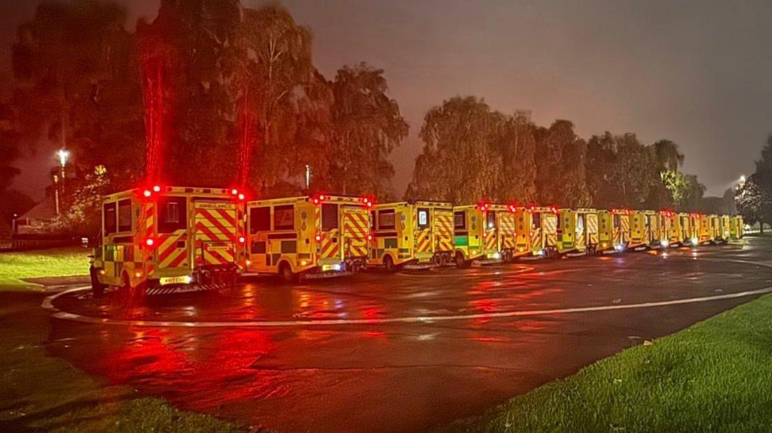 More than ten ambulances lined up in a row on a helipad at night