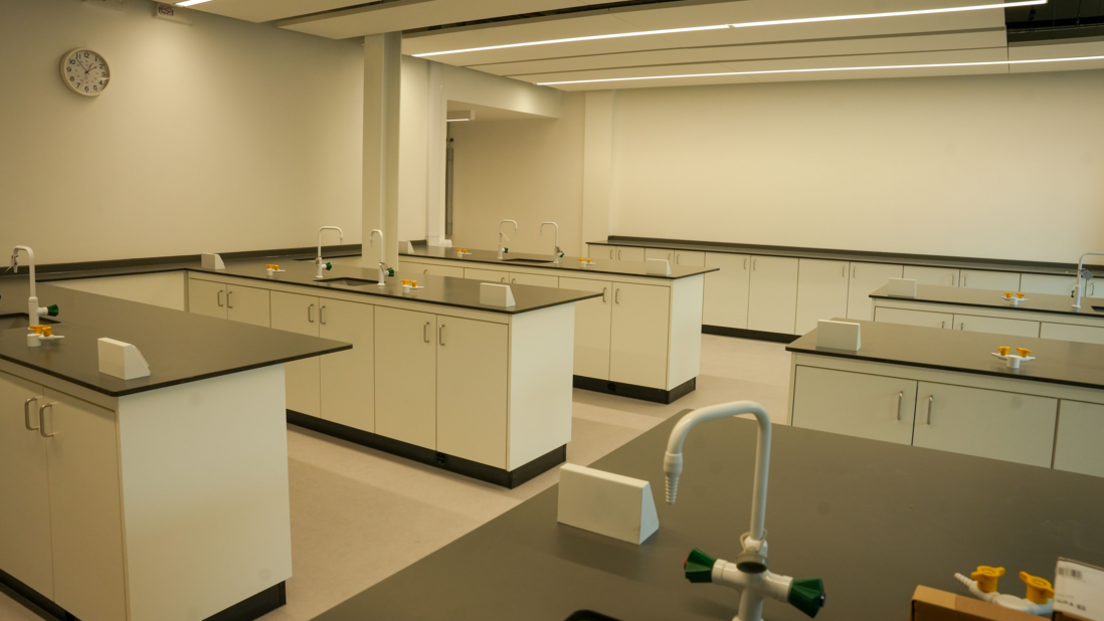 The science laboratory inside the new campus. There are several desks and work tops visible with cream coloured walls and units.