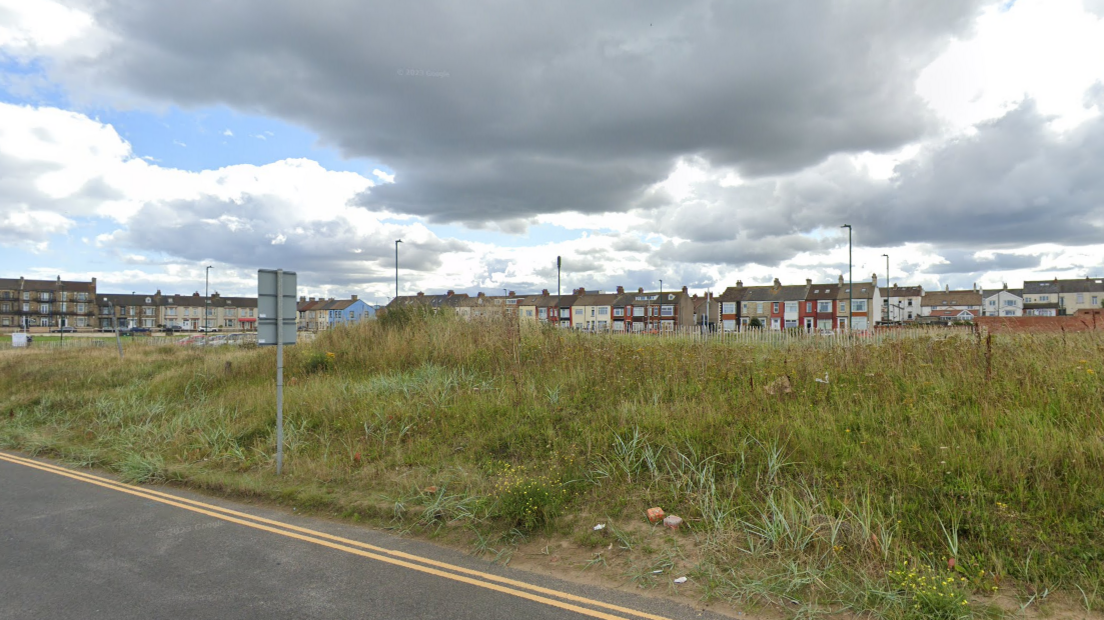 Grassland with rows of houses in the distance