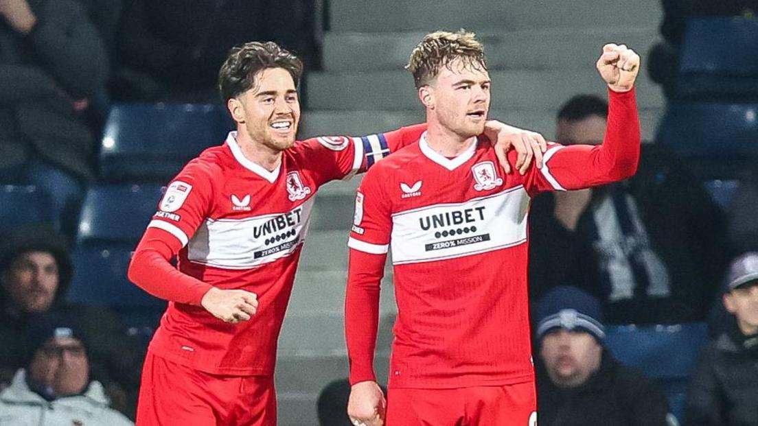 Hayden Hackney, wearing the captain's armband on his left arm, has his left hand on Tommy Conway's left shoulder. Conway has his left fist clenched after Middlesbrough had scored.