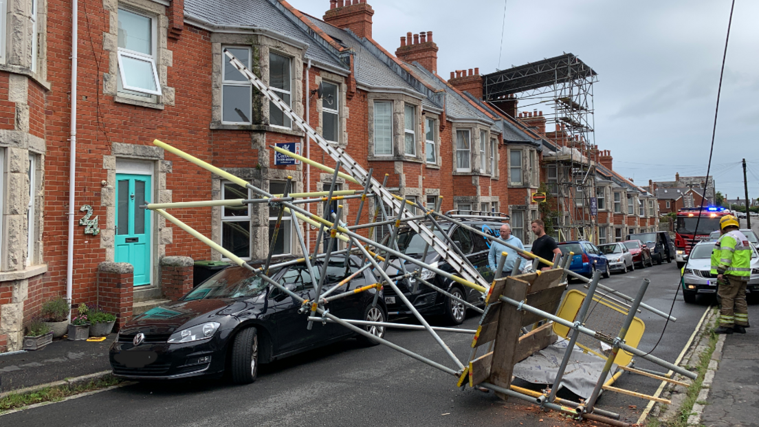 Fallen scaffolding, laying across the road on top of a car. 