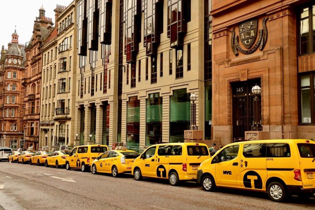 A row of parked yellow taxi's with "NYC" on the side doors, parked outside imposing stone buildings in Glasgow City Centre, styled to look like New York City.