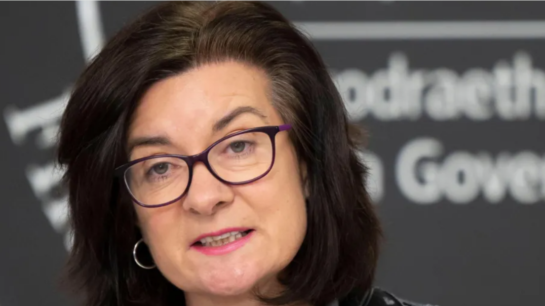 Eluned Morgan, wearing glasses and silver hoop earrings, looking seriously at camera