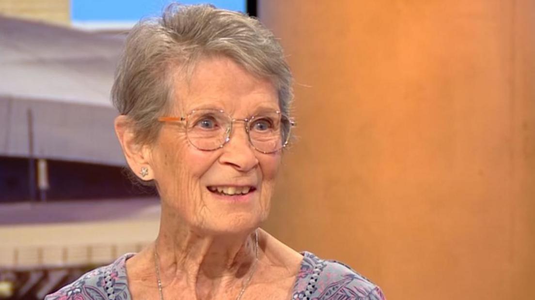 Fiona Castle with short grey hair and glasses and wearing a purple floral dress.