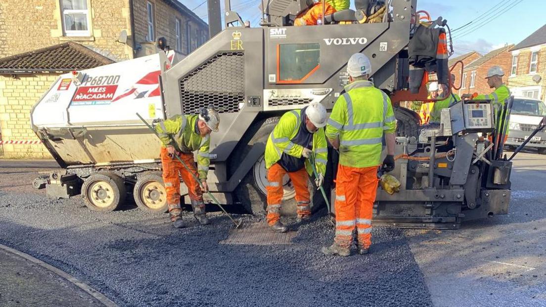 A group of three men resurfacing Ladyfield Road. There is a large vehicle behind them. All are wearing protective gear.