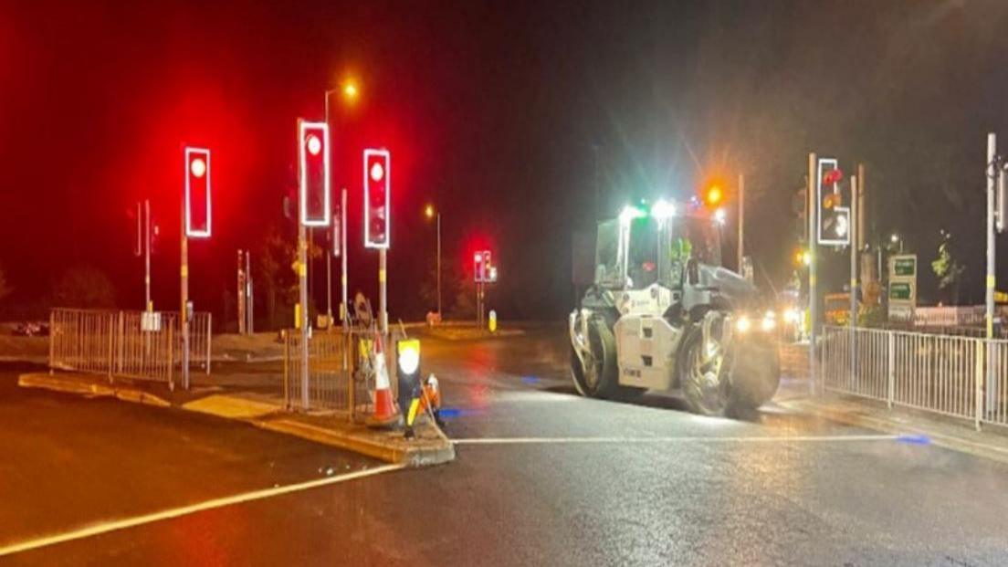 Traffic lights and a small road-flattening vehicle at a crossroads at night