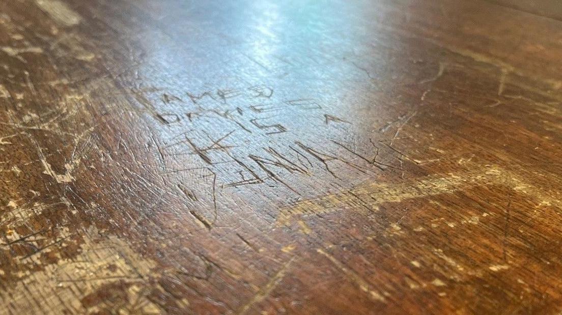 Wooden table with the words "James Davies is a snake" carved into it