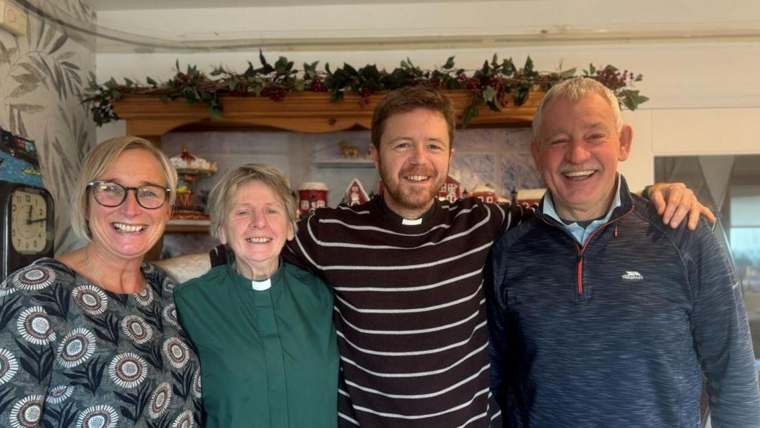 From left to right is a Lorna Brown with short blonde hair and is wearing a patterned top, Reverend Hawthorne-Steele with short hair and a green shirt with clerical collar, Reverend Chris Bennett with brown hair and beard wearing a striped shirt and clerical collar and a man with short grey hair wearing a zip-up fleece. 