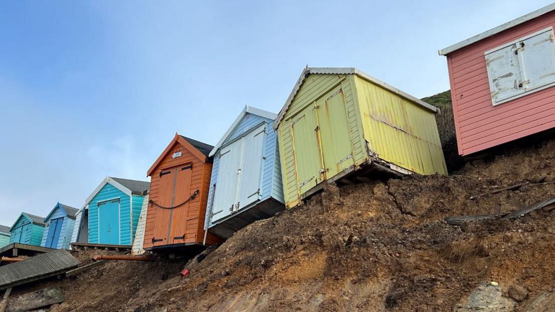 Beach huts battered by bad weather are now teetering on the edge of a cliff