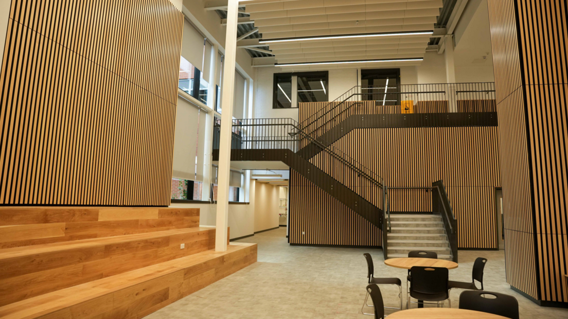 Central atrium inside the new campus has a strong wooden effect throughout with stairs one side and tables and chairs at ground level.