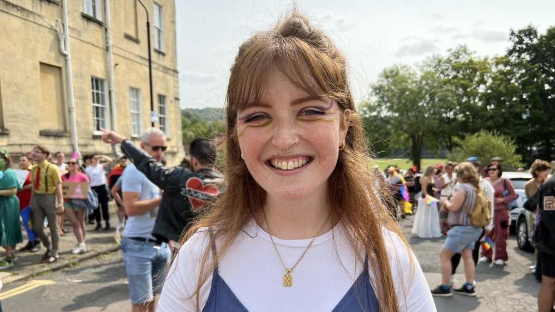 Molly Ridley who has brown hair and is wearing a white top. She is smiling at the camera. Behind her is a group of people who were also involved in the Pride march. 