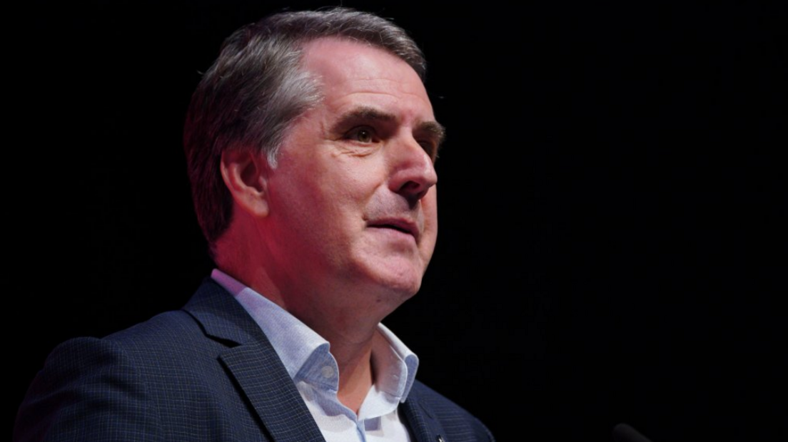 Mayor of the Liverpool City Region Steve Rotheram, in a blue suit and light blue shirt, standing at a podium delivering a speech