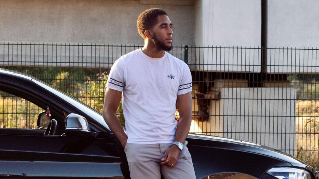 A man standing in front of a black car 