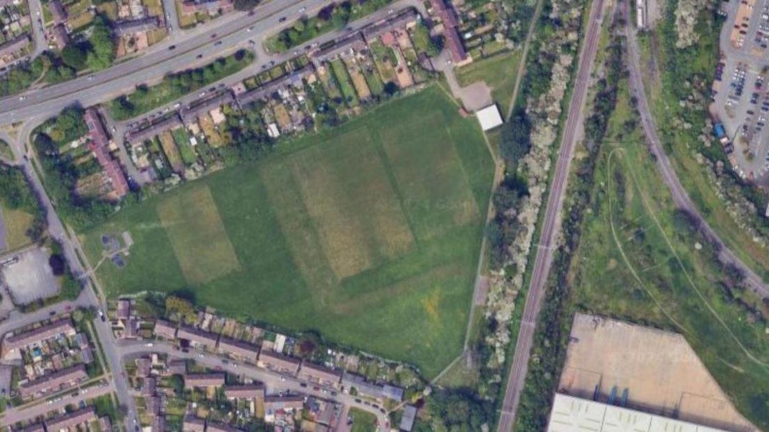 Satellite image showing triangular sports pitch surrounded by trees and houses.