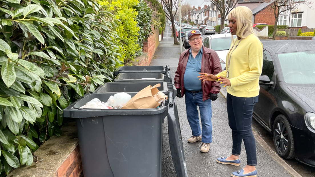 Celia Hibbert and a resident inspect bins lined up along a pavement