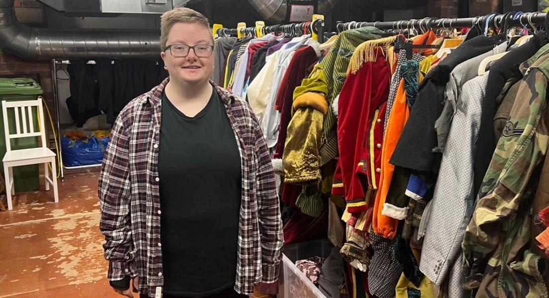 Person standing in front of a rack of theatrical outfits