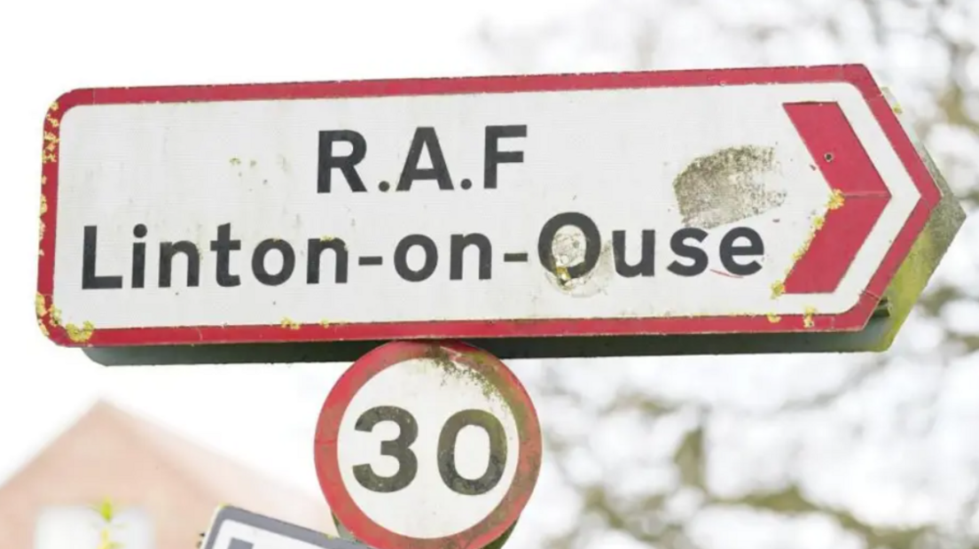 A road sign, white with a red border, with reads 'RAF Linton-on-Ouse.' Underneath it is a separate 30mph road speed sign.