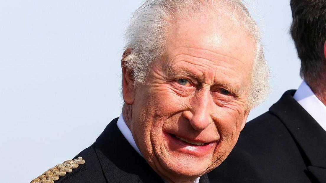 King Charles in naval uniform smiling at the camera