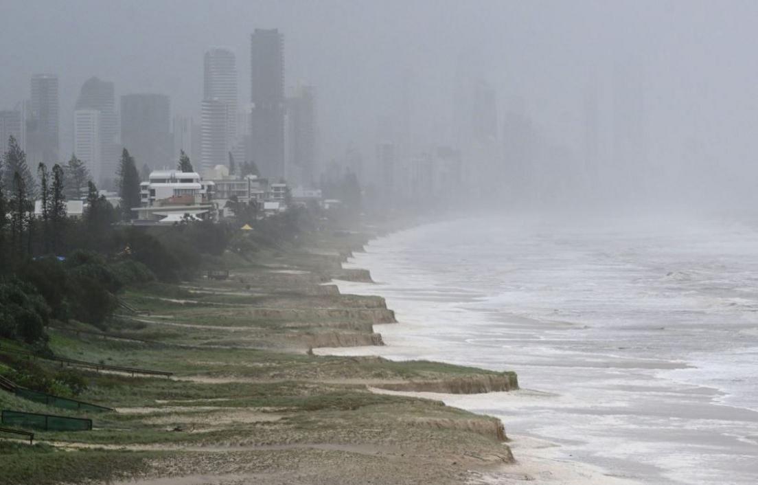 A city skyline with tower blocks partially obscured by heavy cloud and a beach beside a stormy sea 