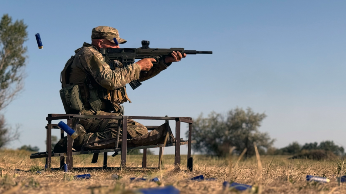 A Ukrainian soldier fires a shotgun in a field during training