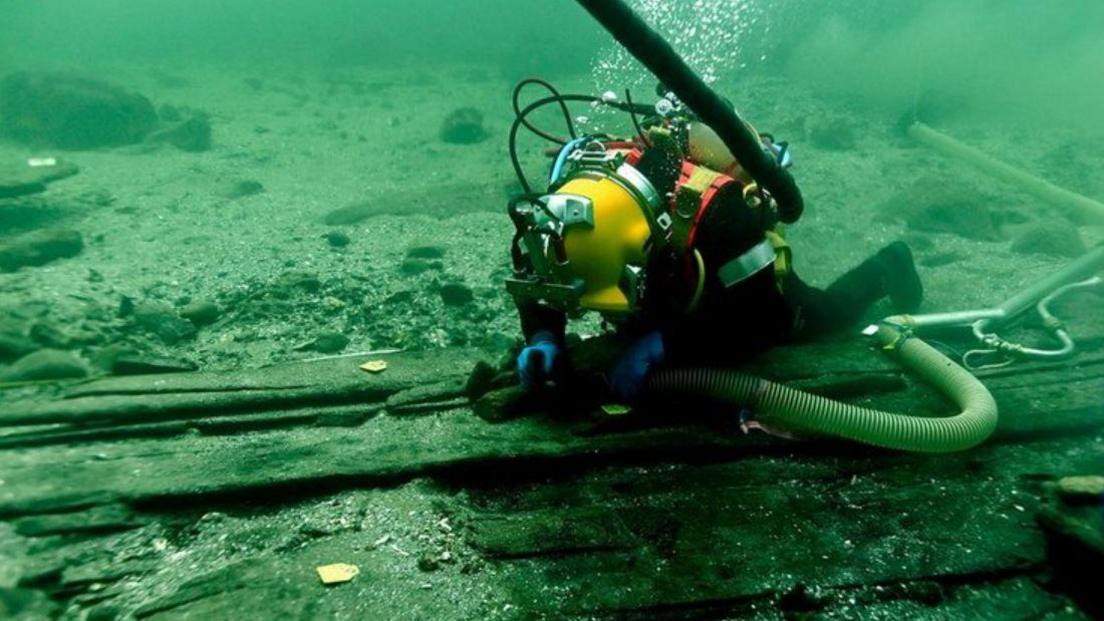 An archaeologist using a special "underwater vacuum cleaners" to remove centuries of sand and silt from the shipwreck.