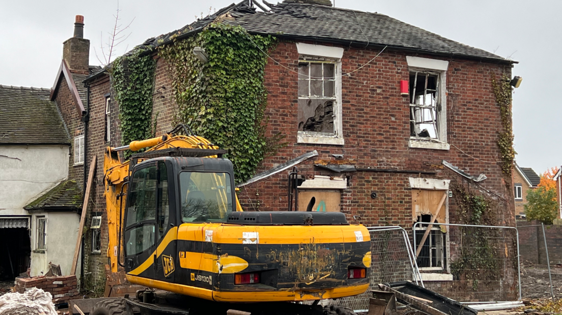 A mechanical digger outside a wreck of a house